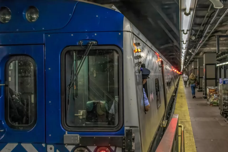 New York City subway train at station with operator looking back toward platform.
